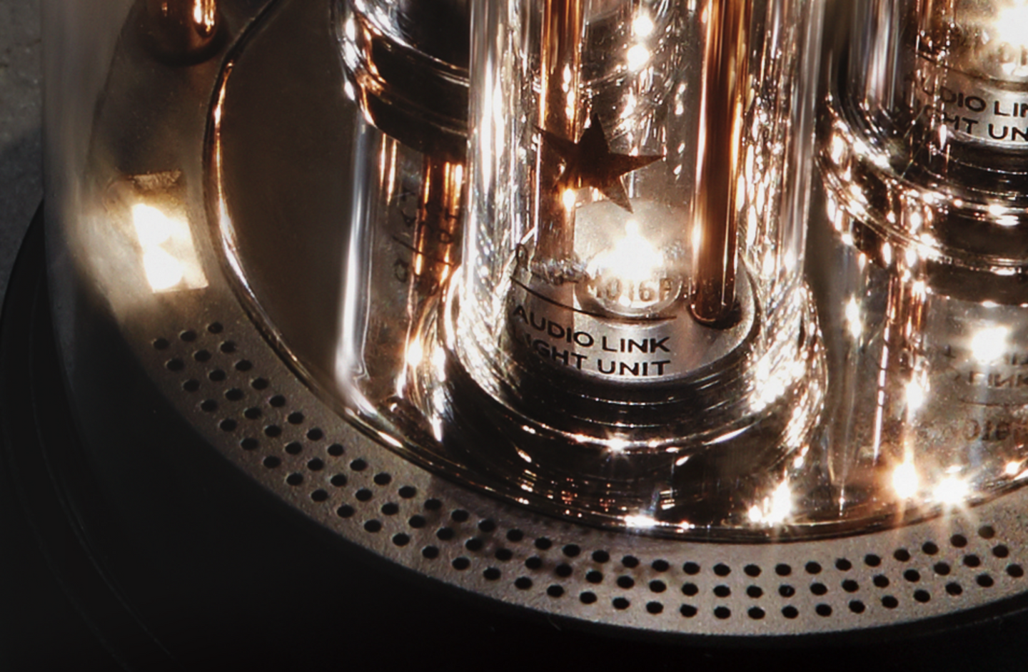 Macro shot of the metallic base of BALMUDA The Speaker with text labeled on the tube: 'AUDIO LINK LIGHT UNIT'.