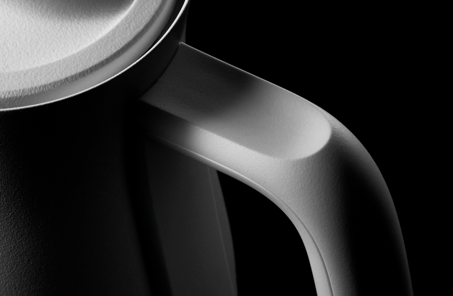 A close-up of the white BALMUDA kettle’s handle, emphasizing the textured finish and ergonomic design.