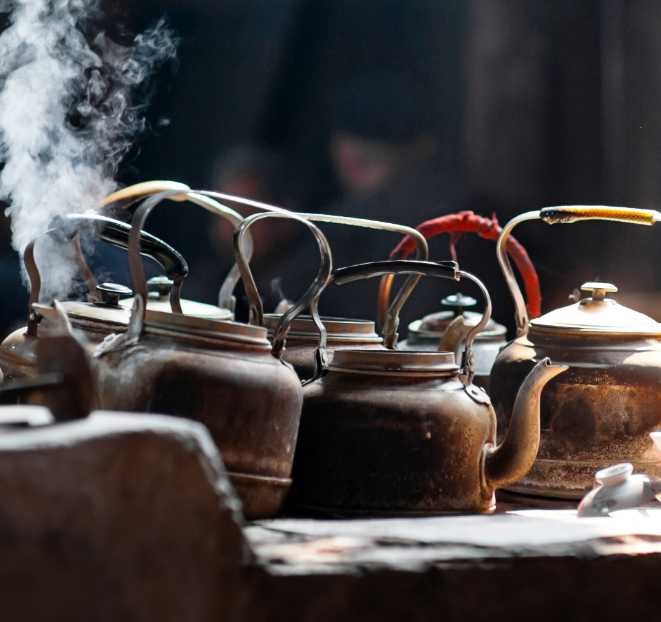Vintage kettles with aged patina, some steaming, lined up over an open fire, evoking an old-world tea-making experience.