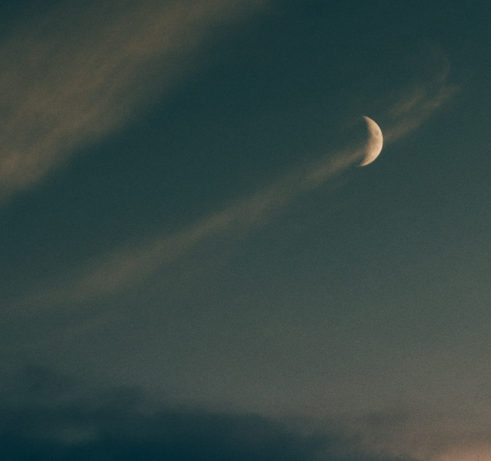 The moon hangs in the twilight sky, surrounded by drifting clouds that add a dreamy, atmospheric feel.