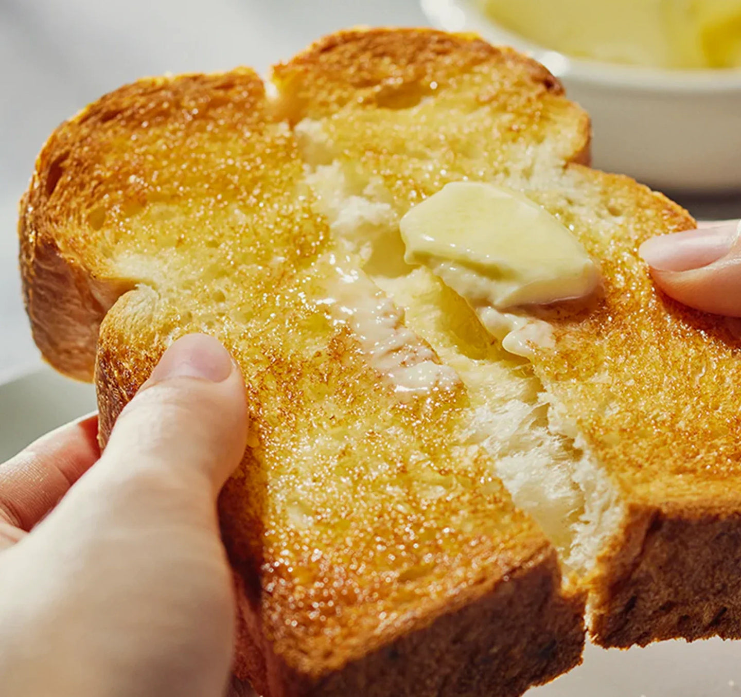 Buttered toast being pulled apart, revealing its fluffy interior and glistening, melted butter.