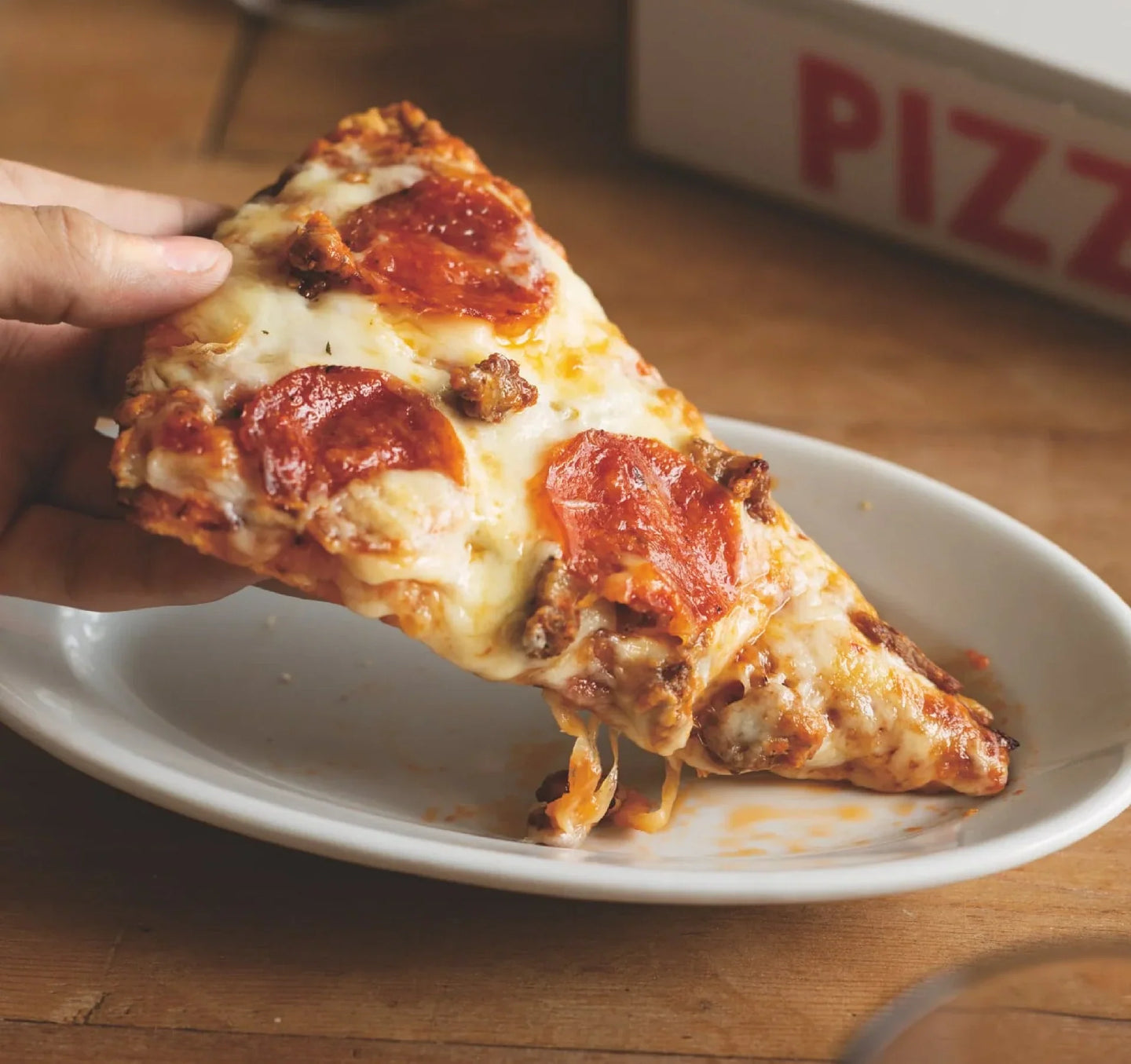 Freshly toasted pizza with crispy pepperoni, sausage, and melted cheese, served on a white plate.