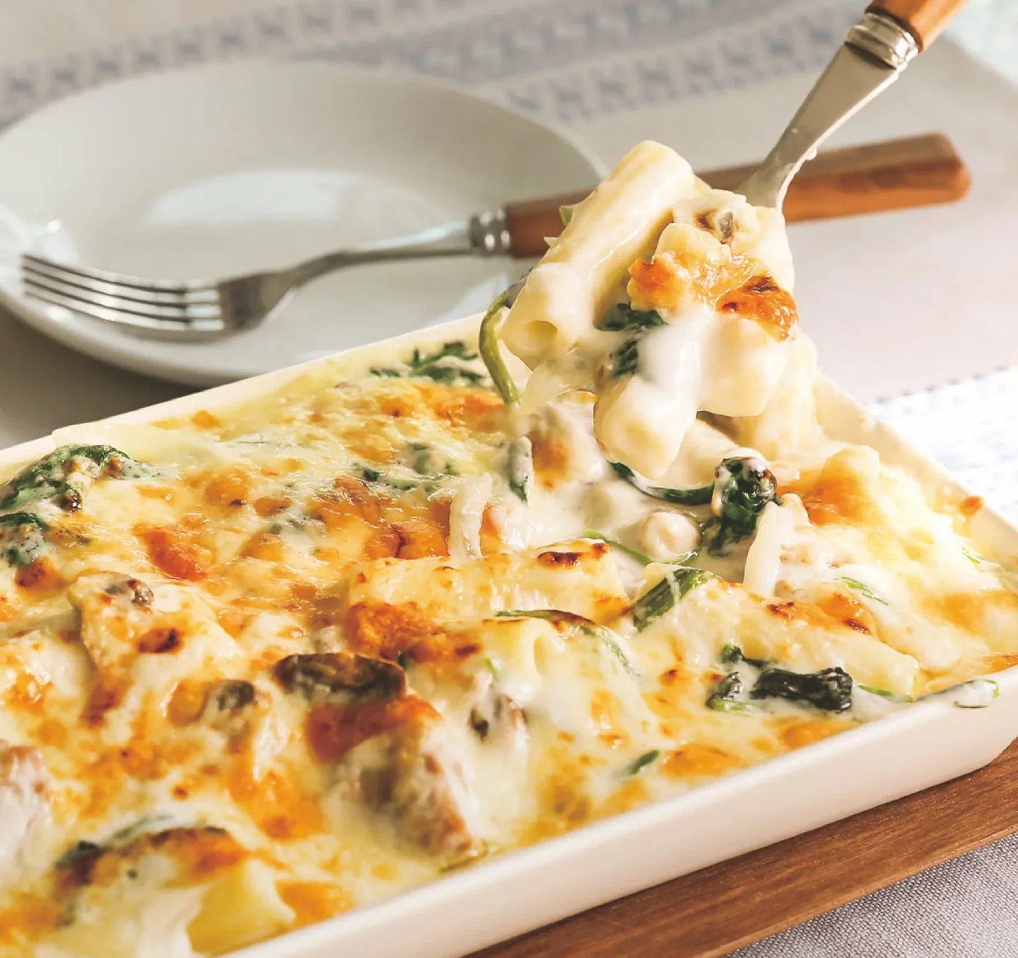 Close-up of a cheesy pasta bake with rigatoni, spinach, and a rich white sauce, served in a white ceramic dish.